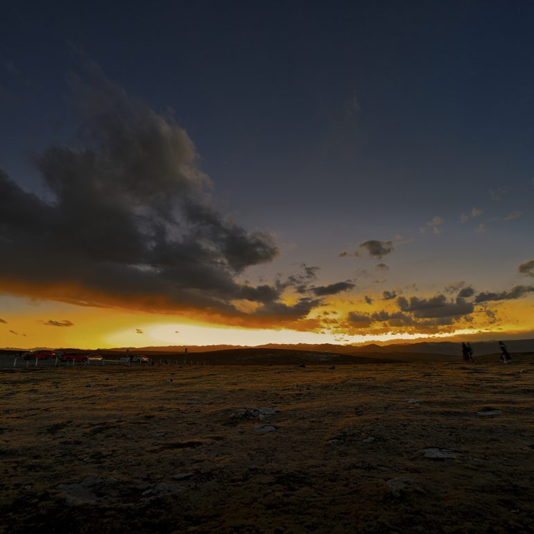 As the sun dips below the horizon, the sky erupts in a symphony of fire. Standing here, in the middle of nowhere, you realize that some moments are too grand for words. Just the wind, the earth, and the endless chase for beauty.